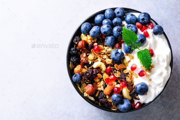 Tasty homemade granola, yogurt, fresh organic berries, pomegranate, mint on grey concrete background - Stock Photo - Images