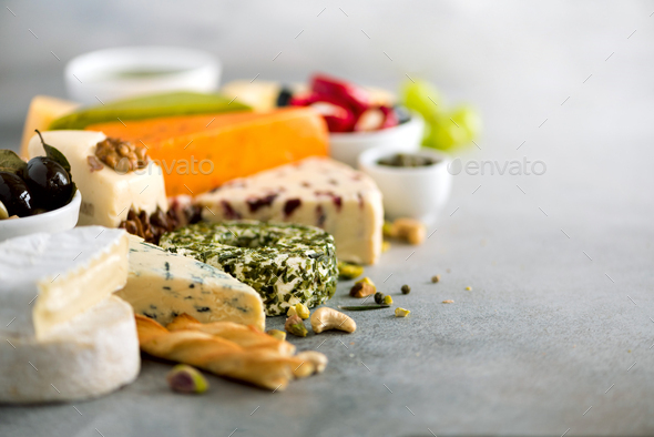 Assortment of hard, semi-soft and soft cheeses with olives, grissini bread sticks, capers, grape, on - Stock Photo - Images