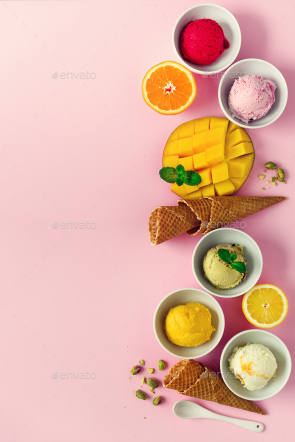 Ice cream balls in bowls, waffle cones, berries, orange, mango, pistachio on pink shabby chic - Stock Photo - Images