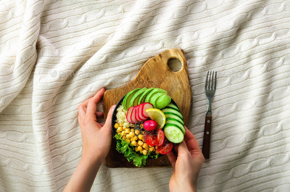 Girl in white jeans holds in hands fork, vegan breakfast meal in bowl with avocado, quinoa, cucumber - Stock Photo - Images