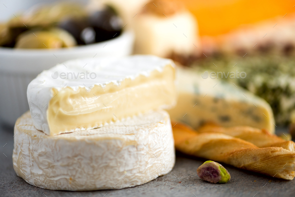 Assortment of hard, semi-soft and soft cheeses with olives, grissini bread sticks, capers, grape, on - Stock Photo - Images
