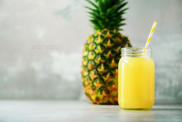 Glass jar of pineapple smoothie and whole fruit on gray background. Copy space. Summer, holiday - Stock Photo - Images