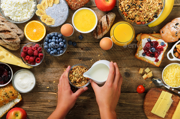 Girl cooking breakfast - granola with yogurt, fruits, berries, milk, yogurt, juice, cheese. Top view - Stock Photo - Images