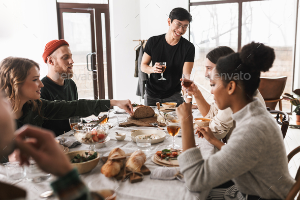 Young cheerful asian man in eyeglasses and black T-shirt holding glass of wine saying toast - Stock Photo - Images