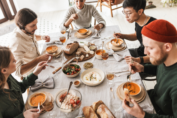 Top view of attractive international friends sitting at the table full of food eating together - Stock Photo - Images