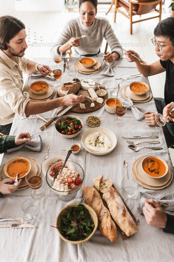 Top view of international friends sitting at the table full of food dreamily eating together - Stock Photo - Images