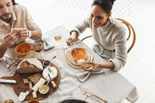 Smiling african american woman sitting at the table eating cream soup with slice of bread - Stock Photo - Images