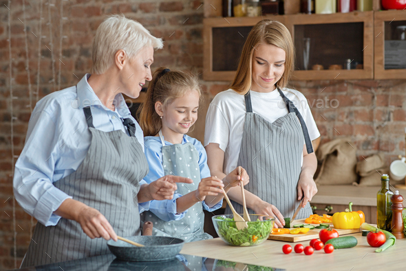 Cute little girl mixing salad under mom and granny supervision