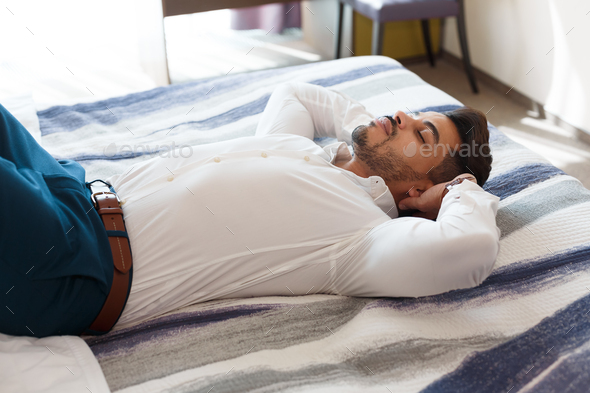 Peaceful businessman resting after hard day on hotel bed