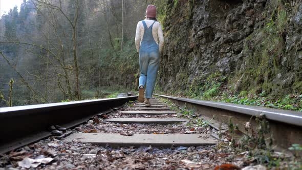 Young Woman in Denim Overall is Walking on Train Rail Alone