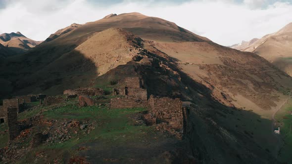 Amazing aerial view of abandoned village, drone flies between stony buildings, mountain summit back alt
