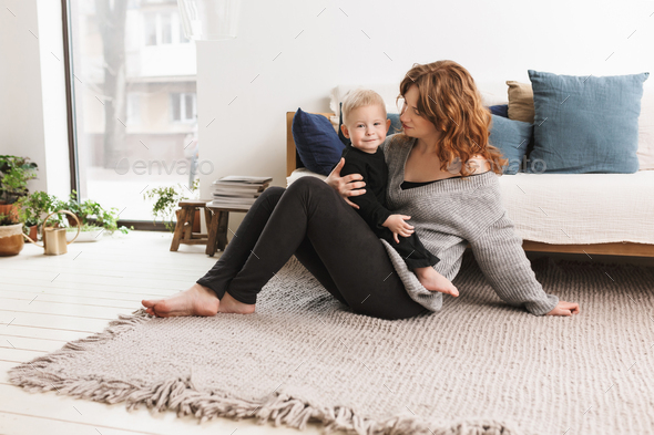 Young beautiful woman sitting on floor holding her little handsome smiling son - Stock Photo - Images