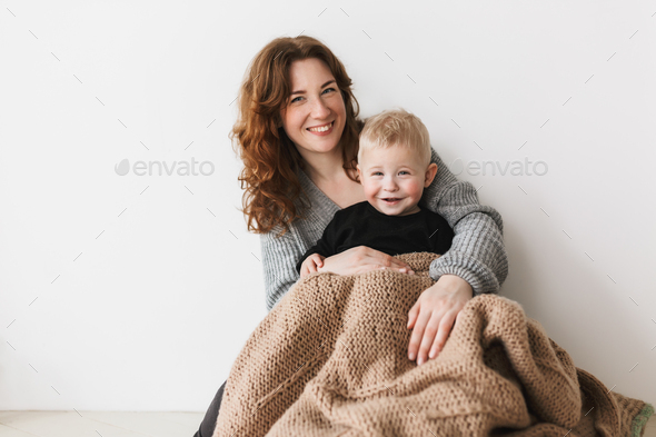 Young beautiful smiling mom with red hair in knitted sweater sitting on floor with her little son - Stock Photo - Images