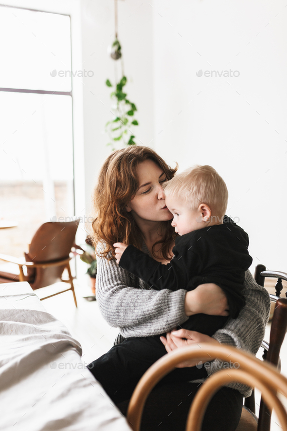 Young beautiful woman in knitted sweater dreamily kissing her little son - Stock Photo - Images