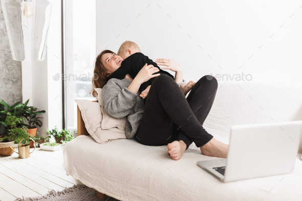 Young cheerful woman on sofa happily hugging her little son - Stock Photo - Images