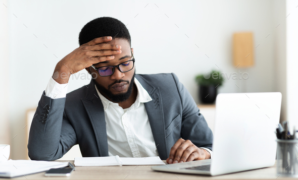 Tired african businessman sitting at workplace frustrated by business failure