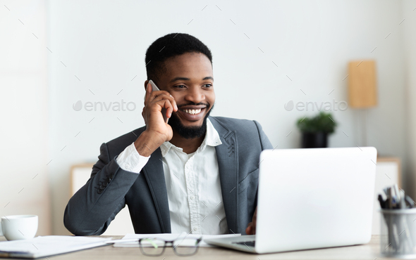 Happy african american employee talking on cellphone at office
