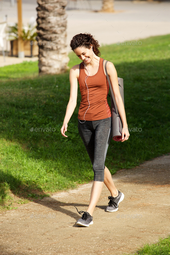 happy young woman walking to yoga lesson in park