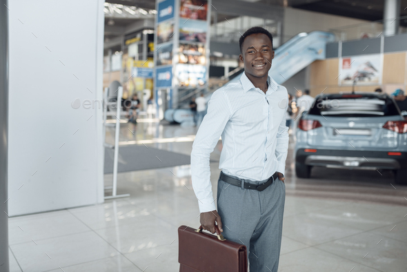 Smiling businessman holds briefcase, car showroom