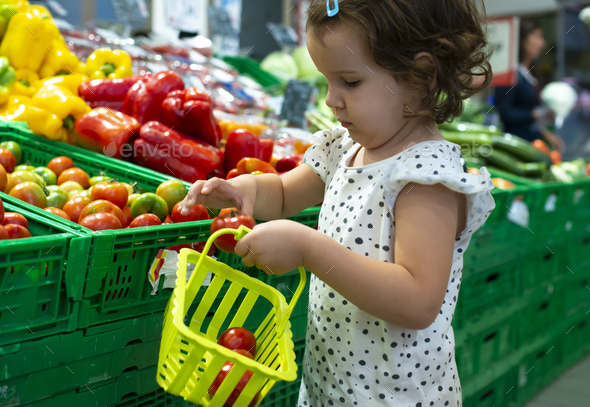 Little girl buying tomatoes in supermarket. Child hold small bas - Stock Photo - Images