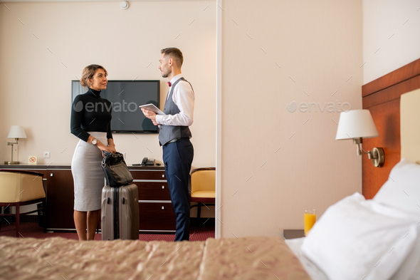 Young elegant businesswoman with suitcase and handbag talking to porter - Stock Photo - Images