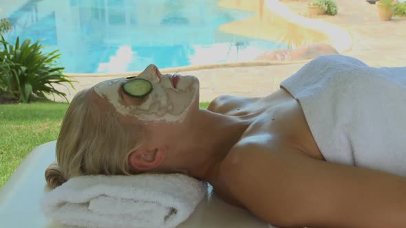 MS OF A WOMAN WEARING A FACE MASK AND TAKING SLICES OF CUCUMBER OFF HER EYES alt