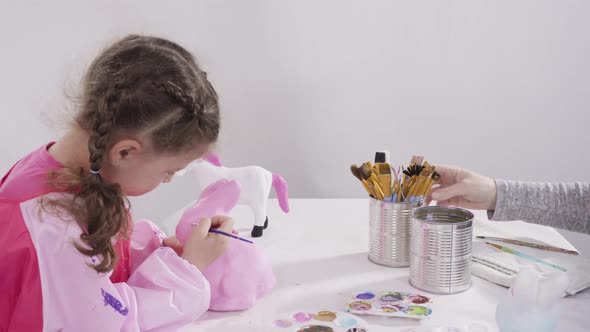 Little girl painting paper mache figurines with acrylic paint  for her homeschooling art project. alt