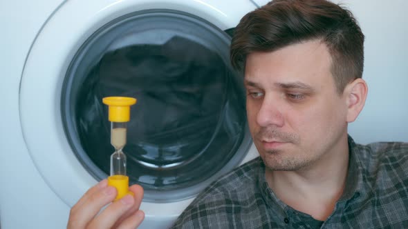 Man with Sandglass is Waiting the Washing Machine with Grey Bedspread Inside It