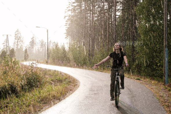 A woman riding a bike and enjoying a warm summer rain - Stock Photo - Images