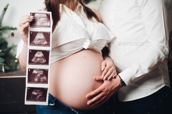 Crop of Pregnant woman posing with man, holding ultrasound pictures - Stock Photo - Images