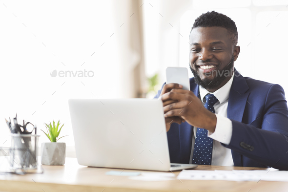 Cheerful businessman chatting with friends on phone, working in office