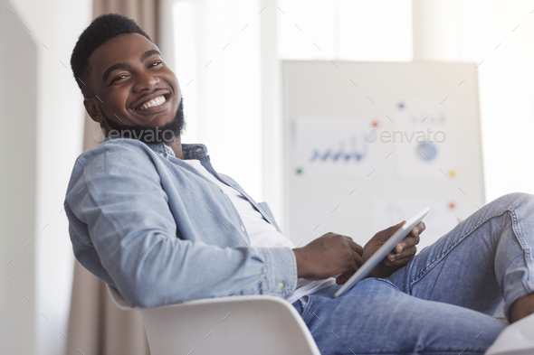 Smiling african american guy sitting at work with digital tablet