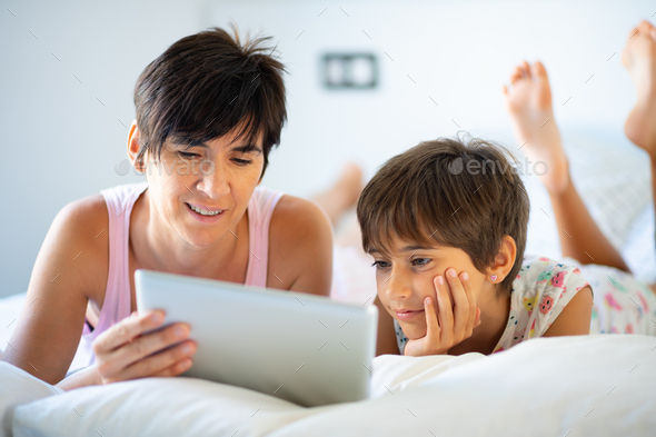 Middle-age mother with her eight years daughter using digital tablet in bedroom