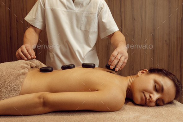 Male masseur puts stones on back of slim woman - Stock Photo - Images