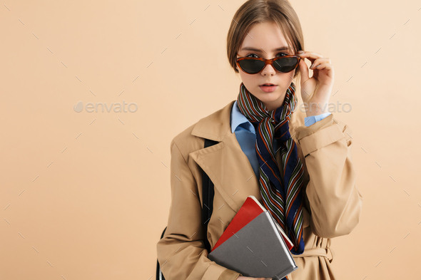 Young stylish dreamy girl in trench coat and sunglasses with notepad curious looking in camera - Stock Photo - Images