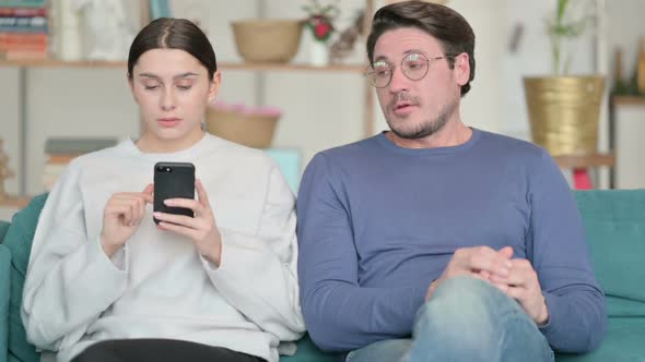 Hispanic Man Feeling Angry Near Female Partner Busy with Smartphone alt