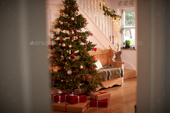 Hallway Of Home Decorated For Christmas With Tree And Presents Viewed Through Open Door