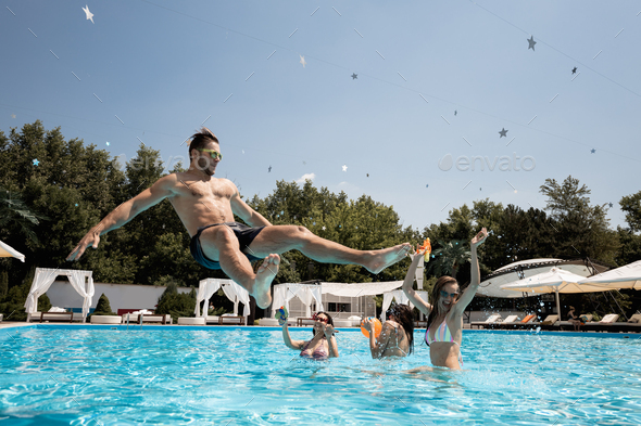 Company of young merry girls and guy relaxing in the swimming pool, jumping in the water and playing - Stock Photo - Images