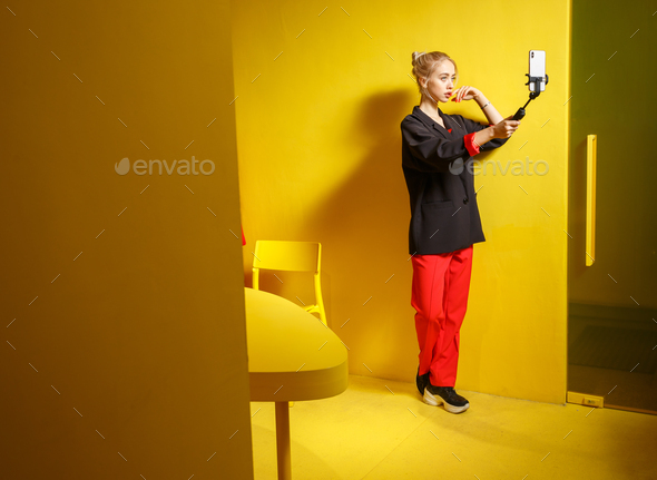 Fashion young girl blogger dressed in red trousers and black jacket takes a selfie on her smartphone - Stock Photo - Images