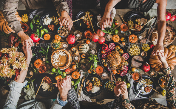 Family or friends praying holding hands at Thanksgiving celebration table