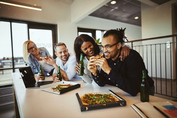 Laughing businesspeople having pizza and beer after work
