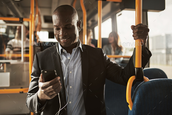 Young African businessman standing on a bus listening to music