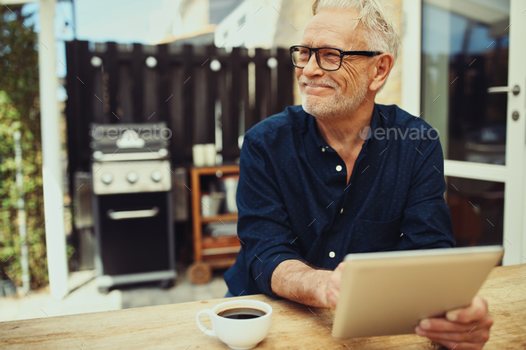 Smiling senior man sitting outside with a coffee and tablet - Stock Photo - Images