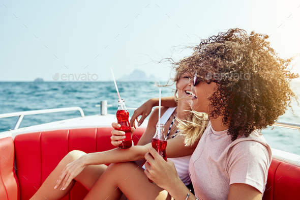 Laughing friends enjoying drinks while sitting on a boat - Stock Photo - Images