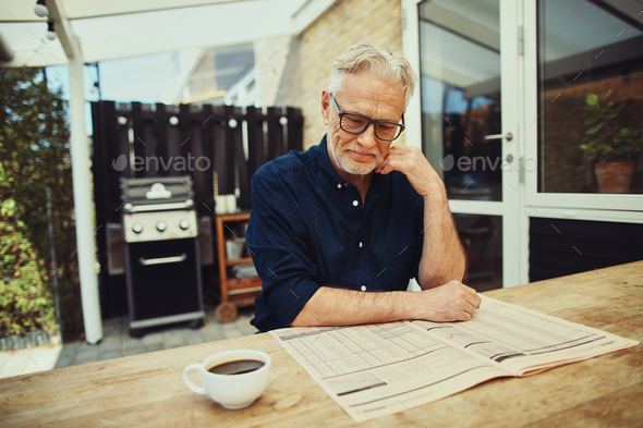 Senior man drinking coffee and reading a newspaper outside - Stock Photo - Images