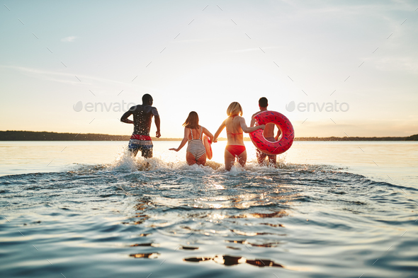 Friends making waves while running into a lake at sunset - Stock Photo - Images