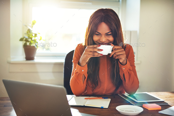 Smiling young female entrepreneur drinking coffee while working from home - Stock Photo - Images