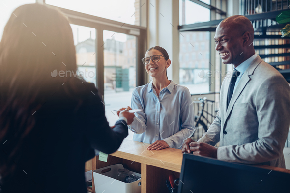 Two smiling hotels guests giving their reservation to reception - Stock Photo - Images