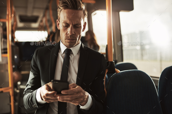 Young businessman standing on a bus sending text messsages
