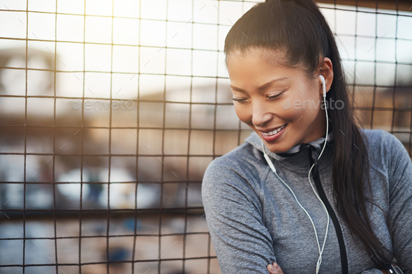 Asian woman smiling and listening to music before exercising outside - Stock Photo - Images